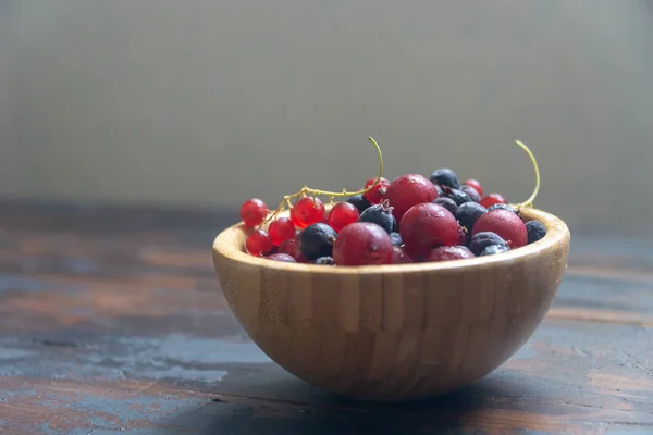 Ripe black and red currants in a wooden bowl on a wooden table. Organic food, berries, harvest season. — Stock Photo, Image