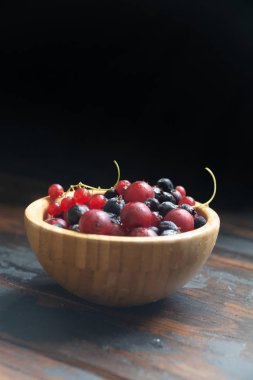 Ahşap bir masa üzerinde ahşap bir kase olgun siyah ve kırmızı kuş üzümü. Organik gıda, çilek, hasat sezonu.