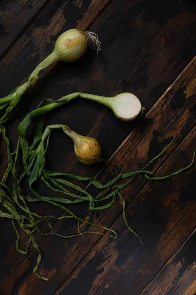 Organikus hagyma levelekkel rusztikus fa asztalra. Élelmiszer-háttér. Izzó hagyma, zöld rugó. Felülnézet. — Stock Fotó
