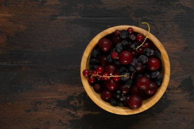 Ahşap bir masa üzerinde ahşap bir kase olgun siyah ve kırmızı kuş üzümü. Organik gıda, çilek, hasat sezonu.