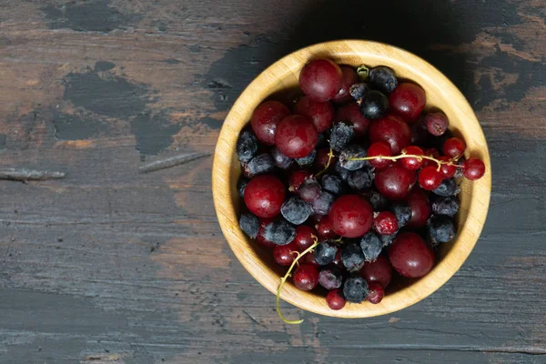 Ripe black and red currants in a wooden bowl on a wooden table. Organic food, berries, harvest season. — Stock Photo, Image