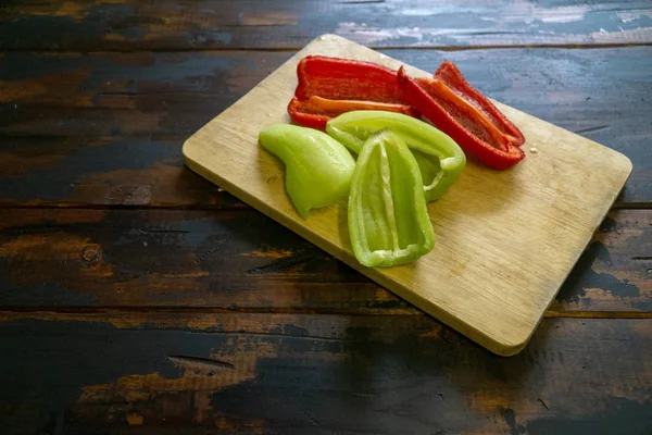 Rote und grüne Paprika auf einem Schneidebrett in Scheiben schneiden. Bio-Lebensmittel und Kochen. — Stockfoto