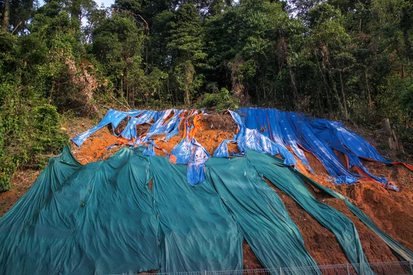 Hangsicherung mit riesiger Plastikfolie zur Vermeidung von Bodenerosion bei Regen. Bunte Plastikdeckel liegen am Hang. — Stockfoto