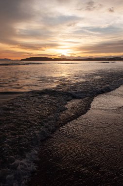 Deniz manzaralı plaj manzarasında gün batımı, bulutlar ve dalgalar. Doğa güzelliği.