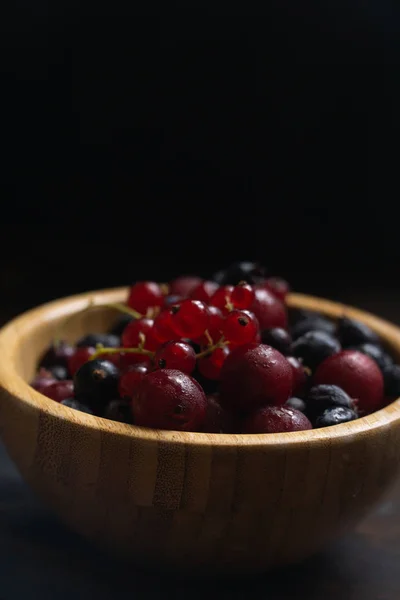 Grosellas maduras negras y rojas en un tazón de madera sobre una mesa de madera. Alimentos orgánicos, bayas, temporada de cosecha . — Foto de Stock