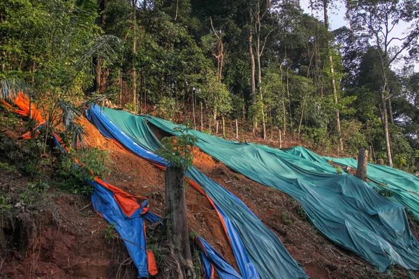 Hangsicherung mit riesiger Plastikfolie zur Vermeidung von Bodenerosion bei Regen. Bunte Plastikdeckel liegen am Hang. — Stockfoto