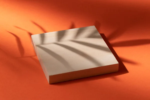 Wooden podium on orange background with the shadow of a palm leaf — Stock Photo, Image