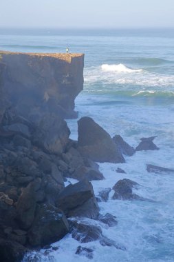 Bir balıkçı Amoreira beach (Aljezur), Costa Vicentina, Algarve, Portekiz yakınındaki yüksek kayalıklarla yukarıda olta balıkçılığı