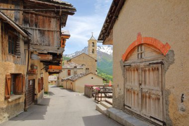 Geleneksel ahşap evler ve Saint veran köyünde kilise, arka planda kar kaplı dağ aralığı, Queyras Regional Tabiat Parkı, Güney Alpleri, Fransa