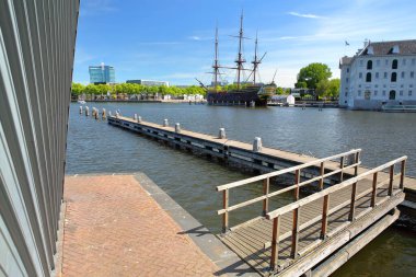 AMSTERDAM, NETHERLANDS - MAI 31, 2020: Ulusal Denizcilik Müzesi 'nin dış cephesi, solunda Hollanda Doğu Hindistan Şirketi' nin 18. yüzyıldan kalma bir kargo gemisi olan Ship Amsterdam 'ın bir kopyası (1985) yer almaktadır.
