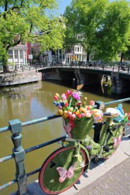 AMSTERDAM, NETHERLANDS - MAI 29, 2020: Brouwersgracht kanalı boyunca yer alan yapay ot, kelebekler ve renkli çiçeklerle süslenmiş bir bisiklet