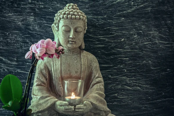 Buddha statue with candle in hands and pink orchid flower. Copy space