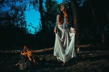 Etnik kıyafetlerle, şenlik ateşinin yanında bir kafa üzerinde chaplet ile kadın. Pagan tatil konsepti.