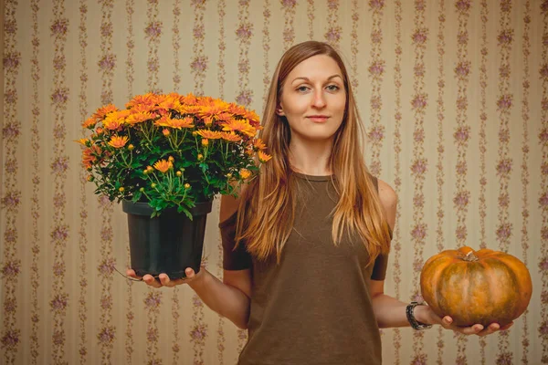 a girl holds flowers in one hand and a pumpkin in the second