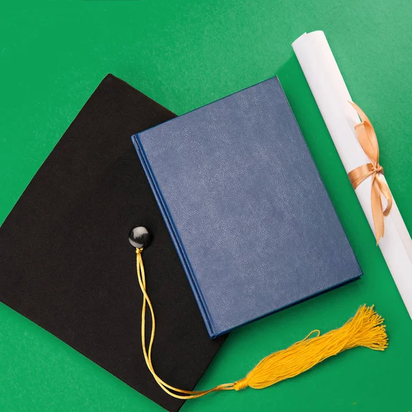 Vista superior del libro, mortero de graduación y diploma en verde - foto de stock