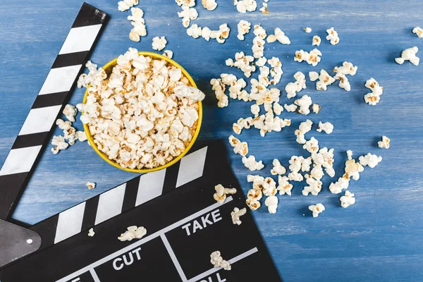 Erhöhte Ansicht von Popcorn-Eimer und Filmklöppel auf blau — Stockfoto