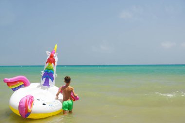 Mutlu küçük çocuk Akdeniz sahilinde dalgalar halinde tek boynuzlu atla yüzüyor. Guardamar, İspanya