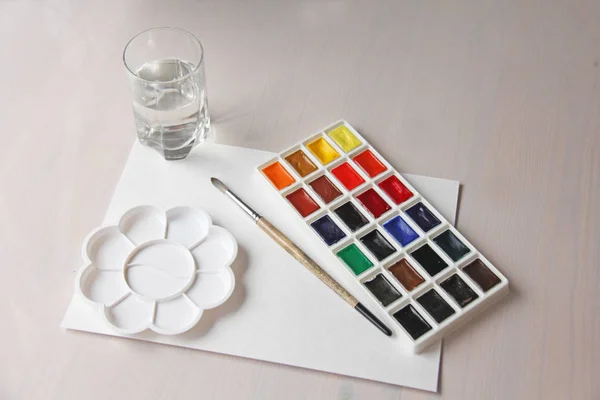 Watercolors, brushes, palette, white sheet of paper and a glass — Stock Photo, Image