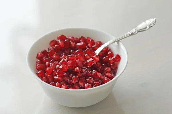 Granos de granada madura roja yacen en un tazón blanco con una cuchara . — Foto de Stock