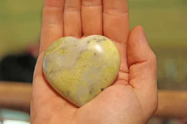 La mano tiene un cuore fatto di pietra naturale giadeite gialla. Hea. — Foto Stock