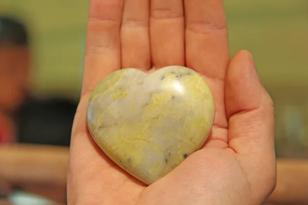 Ręka trzyma serce wykonane z naturalnego kamienia żółtego jadeite. Hea — Zdjęcie stockowe