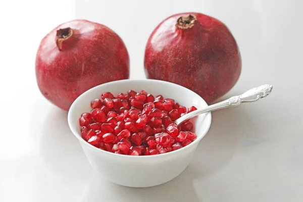 Körner roter reifer Granatäpfel liegen in einer weißen Schüssel mit einem Löffel. — Stockfoto
