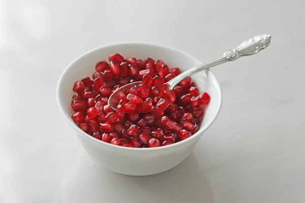 Granos de granada madura roja yacen en un tazón blanco con una cuchara . — Foto de Stock