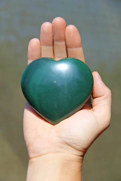 Ręka trzyma serce z naturalnego kamienia zielony Jade. Serce w — Zdjęcie stockowe
