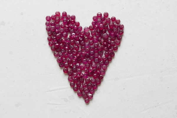 Pedras rubi estão em uma mesa branca na forma de um coração. Natura — Fotografia de Stock