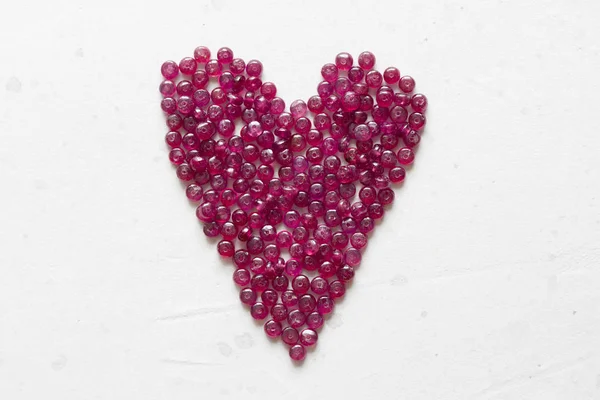 Las piedras de rubí yacen sobre una mesa blanca en forma de corazón. Natura —  Fotos de Stock