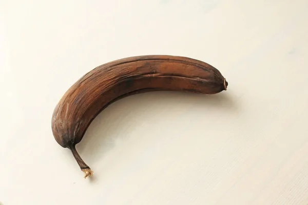 Banana preta estragada. Uma banana podre em um backgrou de madeira branco — Fotografia de Stock