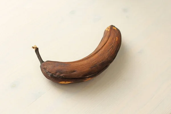 Banana preta estragada. Uma banana podre em um backgrou de madeira branco — Fotografia de Stock