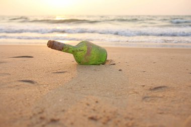 Yeşil cam şişe üzerinde deniz kıyısında içinde bir mesaj ile 