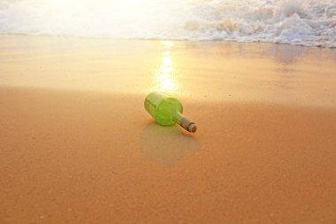 Yeşil cam şişe üzerinde deniz kıyısında içinde bir mesaj ile 
