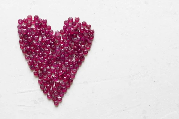 Ruby stones lie on a white table in the shape of a heart. Natura