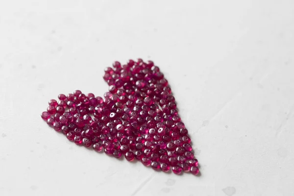 Ruby stones lie on a white table in the shape of a heart. Natura