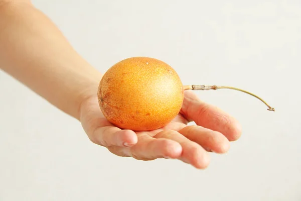 Um maracujá amarelo ou laranja está em uma mão sobre um bac branco — Fotografia de Stock