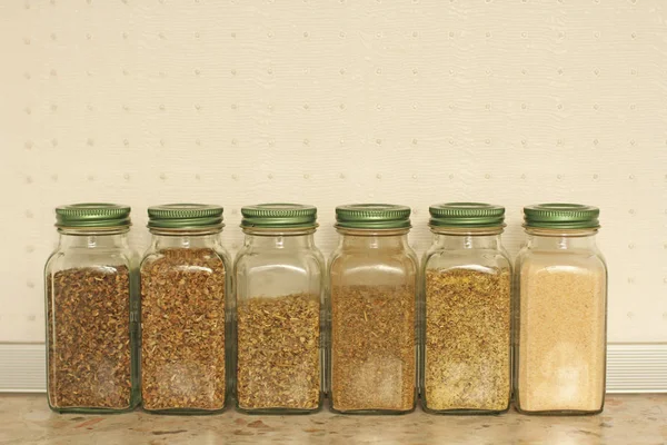 Especias en frascos de vidrio sobre un fondo claro en la cocina. Basilio. — Foto de Stock