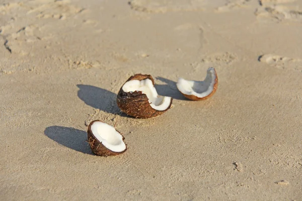 Een open bruine kokosnoot met wit vlees ligt op het strand, op de — Stockfoto