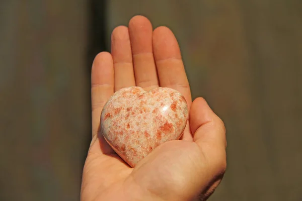 Ręka trzyma serce z naturalnego kamienia roochrosite. Serca — Zdjęcie stockowe