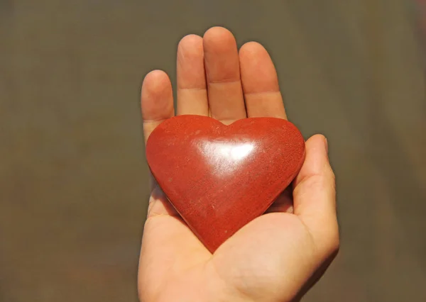 Ręka posiada czerwone lub terakotowe serce wykonane z kamienia naturalnego. — Zdjęcie stockowe