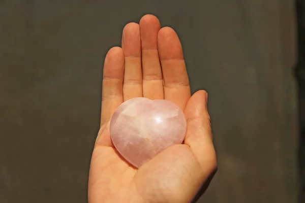 Ręka trzyma serce z kamienia naturalnego kwarcu różowy. Serce w ha — Zdjęcie stockowe
