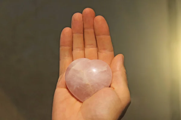 La mano tiene un cuore di pietra naturale quarzo rosa. Cuore in ha — Foto Stock