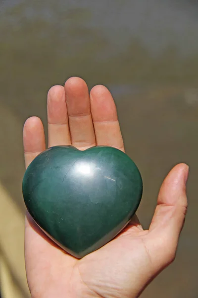 Ręka trzyma serce z naturalnego kamienia zielony Jade. Serce w — Zdjęcie stockowe
