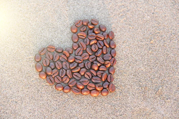 Кофейное сердце. Кофейные зёрна высыпаются на песок. — стоковое фото