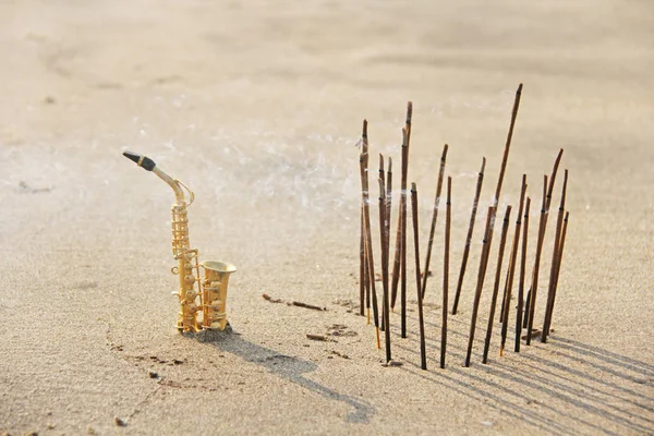 El saxofón alto dorado se encuentra en la arena junto al incienso —  Fotos de Stock