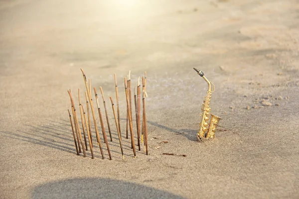 El saxofón alto dorado se encuentra en la arena junto al incienso —  Fotos de Stock