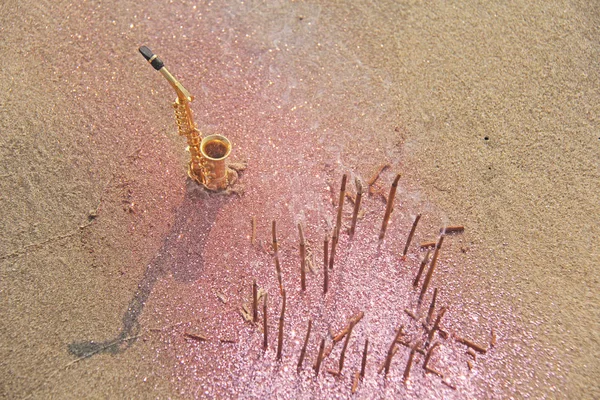 De gouden saxofoon alto staat op het zand naast de fragran — Stockfoto