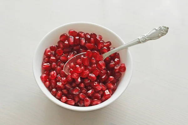 Granos de granada madura roja yacen en un tazón blanco con una cuchara . — Foto de Stock