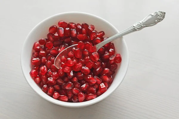 Granos de granada madura roja yacen en un tazón blanco con una cuchara . — Foto de Stock